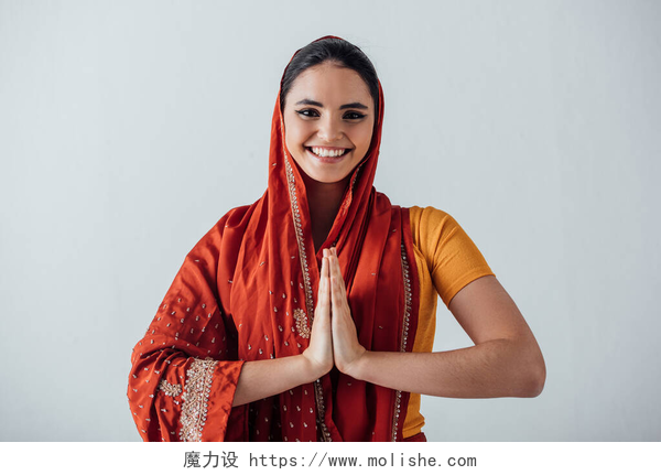 灰色背景前的微笑的印度女人双手合十微笑的印度女人，手牵着手看着灰色的相机